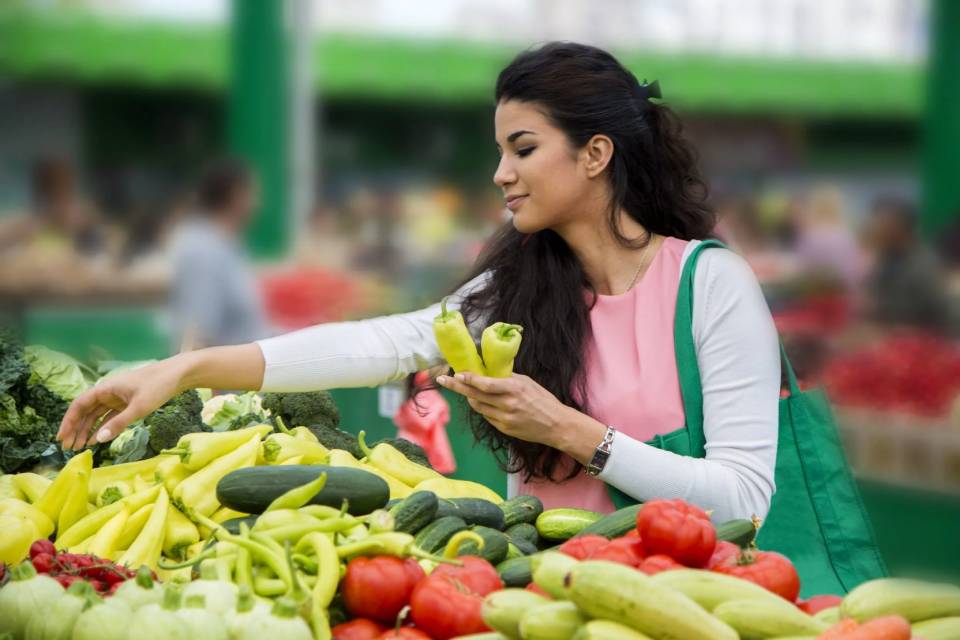  A young woman selects fresh organic peppers from a market stall.